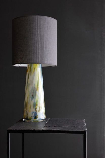 Lampa szklana w cętki na stoliku na tle szarej ściany
