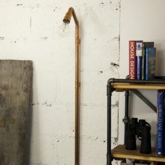 Miedziana lampa ścienna Wand wykonana z rurek hydraulicznych z żarówką Edison. Industrialny design na białej ścianie obok metalowego regału. Minimalistyczny, loftowy styl idealny do surowych, kreatywnych przestrzeni.