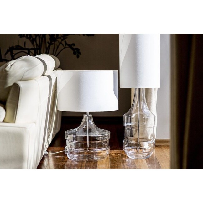 Eleganckie lampy stołowe w stylu hampton z transparentnymi szklanymi podstawami o różnych kształtach i białymi abażurami. Ustawione na drewnianej podłodze obok kremowej sofy. Ponadczasowy design łączący nowoczesną przejrzystość szkła z klasyczną formą abażurów, idealny do nadmorskich i eleganckich wnętrz w stylu hampton, gdzie liczy się jasna kolorystyka i naturalne materiały.