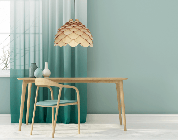 Drewniana lampa wisząca o strukturze przypominającej szyszkę, wykonana z jasnego drewna. Zawieszona nad minimalistycznym drewnianym stołem w miętowym wnętrzu, podkreśla naturalny, skandynawski styl aranżacji przestrzeni.