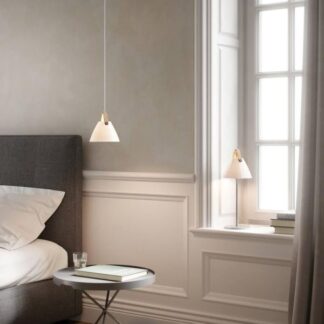 Nowoczesna jasna sypialnia z szarym łóżkiem, minimalistycznymi lampami stożkowymi - wiszącą nad łóżkiem i stojącą na białym parapecie. Wnętrze z beżowymi ścianami, klasycznymi sztukateriami i jodełkową podłogą. Widoczny okrągły stolik nocny z książką.