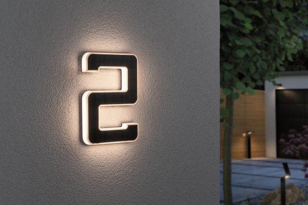 Kinkiet zewnętrzny LED w kształcie cyfry 2 zamontowany na szarej ścianie z podświetleniem.