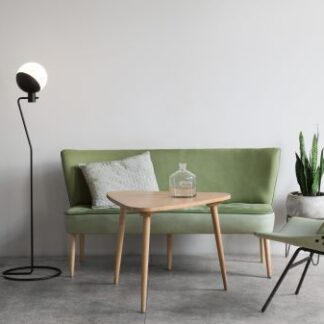 Czarna lampa podłogowa Baluna z białym kulistym kloszem ustawiona w jasnym salonie obok zielonej sofy, drewnianego stolika kawowego i dopasowanego fotela. Po bokach widoczne rośliny doniczkowe na metalowych stojakach. Całość na szarej podłodze.