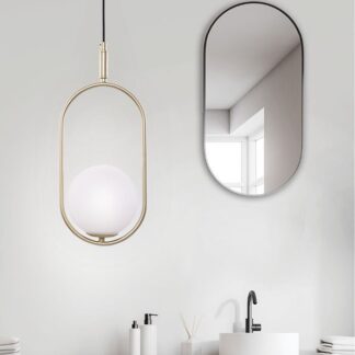 Złota lampa wisząca Cordel z białym kulistym kloszem wewnątrz owalnej, metalowej ramy, zawieszona w minimalistycznej łazience z owlanym lustrem, drewnianą szafką i białą umywalką nablatową.