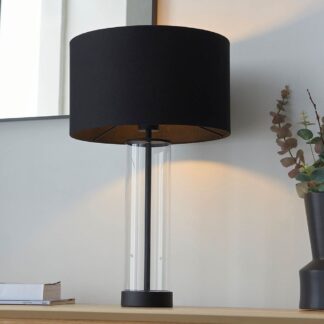 Czarna lampa stołowa Lessina z tekstylnym abażurem i transparentną szklaną podstawą na drewnianym blacie. Elegancki, minimalistyczny design idealny do biura i przestrzeni domowych.