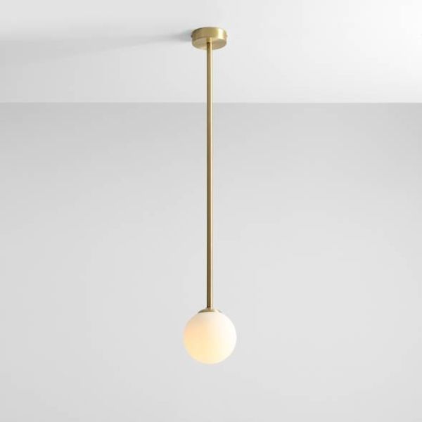 Wisząca lampa Pinne L w kolorze mosiądzu z okrągłym białym kloszem na długim pręcie.