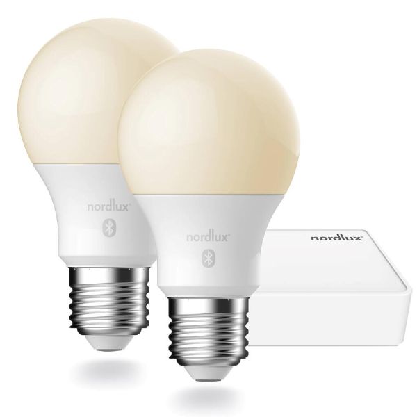 Dwie białe żarówki LED E27 Smart z ciepłym światłem i biały hub sterowniczy Nordlux na białym tle.