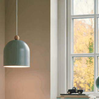 Skandynawska lampa wisząca Gaston w kolorze szałwii z półokrągłym kloszem i drewnianym elementem u góry. Zawieszona w jasnym wnętrzu przy dużym oknie z widokiem na jesienne drzewa.
