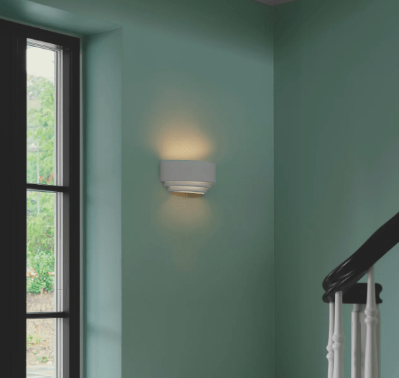 Gipsowy kinkiet Lancio Oblong Nordlux na miętowej ścianie przy schodach. Biała, minimalistyczna lampa ścienna z eleganckim, rozproszonym światłem tworzącym przytulną atmosferę. Nowoczesne oświetlenie dekoracyjne do wnętrz domowych.
