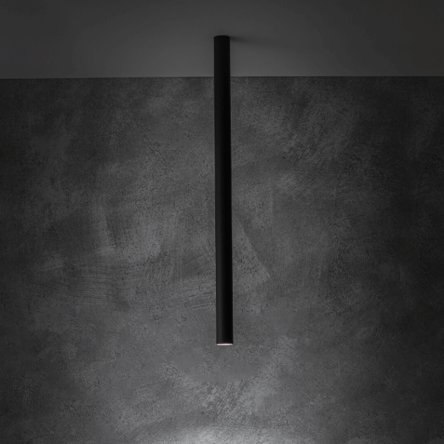 Architektoniczna czarna lampa sufitowa Fourty M w formie smukłej, pionowej tuby (75 cm), tworząca dramatyczny, wąski snop światła na betonowej ścianie, doskonała do akcentowego oświetlenia przestrzeni loftowych.