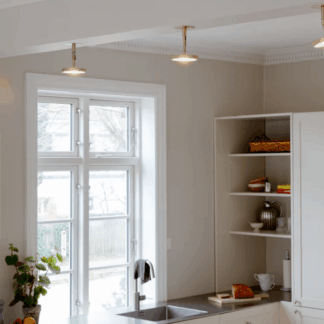 Złote lampy sufitowe LED Asteria Umage w mosiężnym wykończeniu nad białą kuchnią. Minimalistyczne reflektory równomiernie oświetlają przestrzeń roboczą z zlewozmywakiem. Eleganckie rozwiązanie do nowoczesnych wnętrz z klasycznymi elementami.