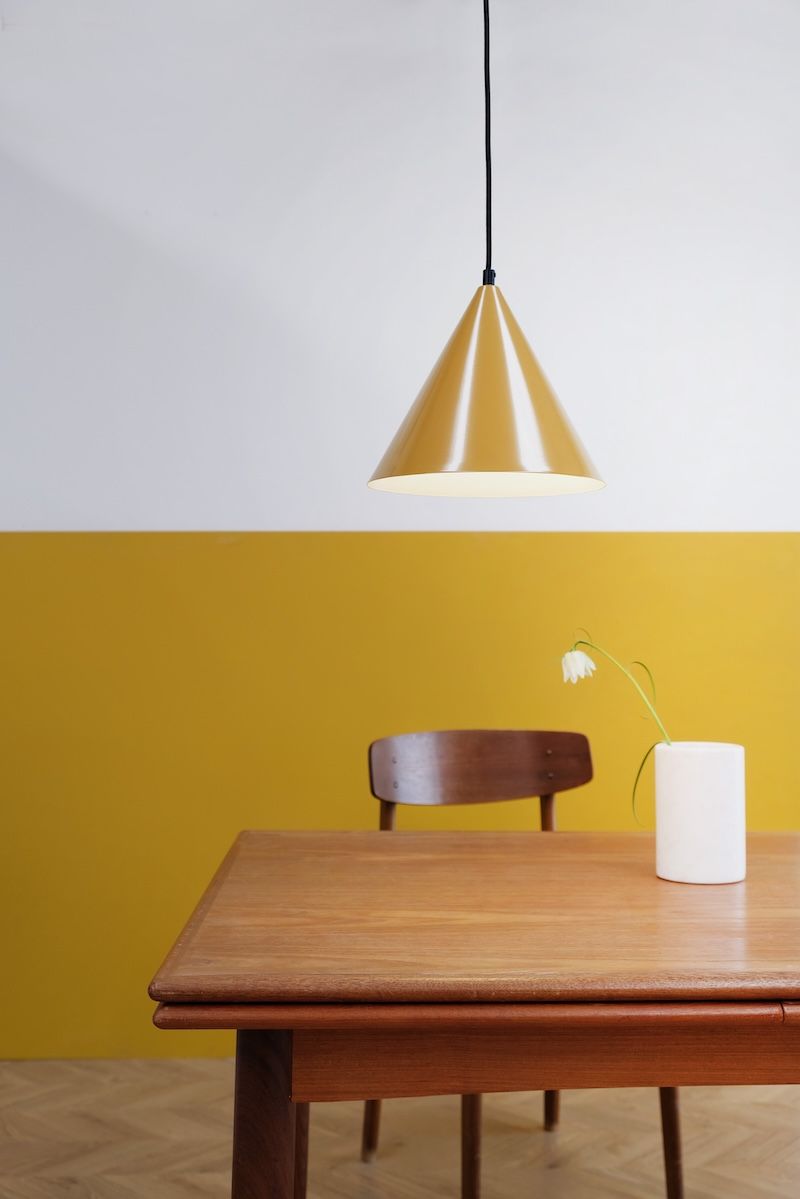 Żółta lampa wisząca w kształcie stożka nad stolikiem Ron od Dyberg Larsen