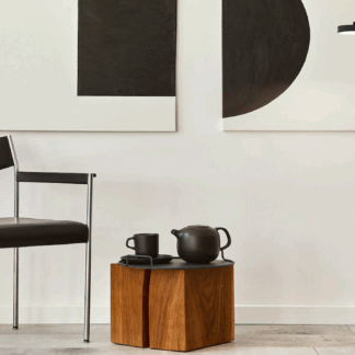 Czarna minimalistyczna lampa podłogowa LED z pionowym słupkiem i poziomym ramieniem w kształcie litery T, ustawiona w nowoczesnym salonie z białymi ścianami, czarno-białymi obrazami, czarnym fotelem i drewnianym stolikiem z ciemną ceramiką.