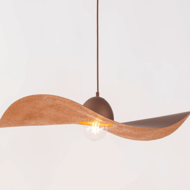 Nowoczesna lampa wisząca w kształcie kapelusza, wykonana z brązowego materiału o fakturowanej powierzchni. Oprawa z ciemnobrązowym mocowaniem i widoczną żarówką Edison. Asymetryczny, stylowy design z dwoma wygiętymi płaszczyznami nadającymi charakterystyczny wygląd. Produkt pokazany na białym tle, idealny do wnętrz w stylu nowoczesnym.