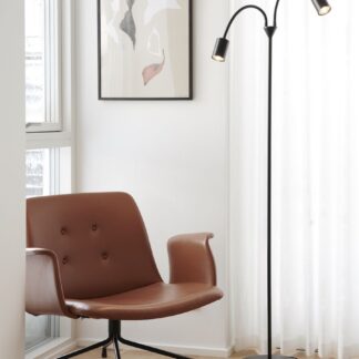 Lampa podłogowa Explore do czytania z dwoma elastycznymi ramionami i czarnymi reflektorami LED. Nowoczesne oświetlenie stojące przy brązowym, skórzanym fotelu w jasnym salonie. Funkcjonalny, minimalistyczny design idealny do kącika czytelniczego.