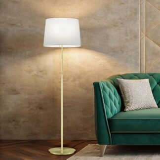 Złota lampa podłogowa Lyon z białym abażurem stojąca przy zielonej pikowanej sofie na tle beżowej teksturowanej ściany i drewnianej podłogi.