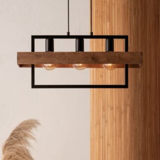 Loftowa lampa wisząca Solvane 3 - połączeniem czarnej metalowej ramy, drewnianej belki i trzech żarówek typu Edison. Zawieszona na tle białej ściany i drewnianego panelu, uzupełniona dekoracyjną trawą pampasową u dołu.