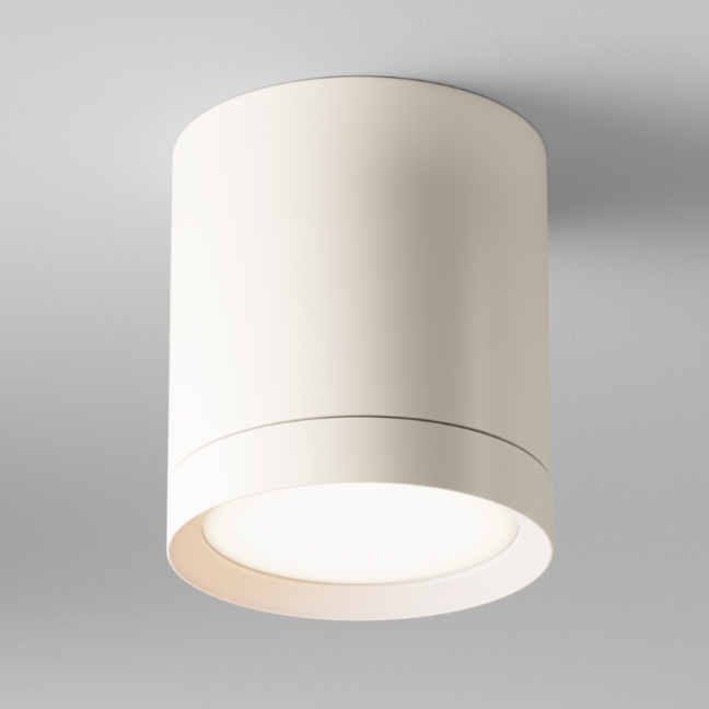 Biała natynkowa lampa sufitowa Hoop o cylindrycznym kształcie z wewnętrznym źródłem światła, zamontowana na jasnym suficie. Minimalistyczna oprawa z charakterystycznym okrągłym wycięciem na dolnej krawędzi, przez które wydostaje się ciepłe światło.