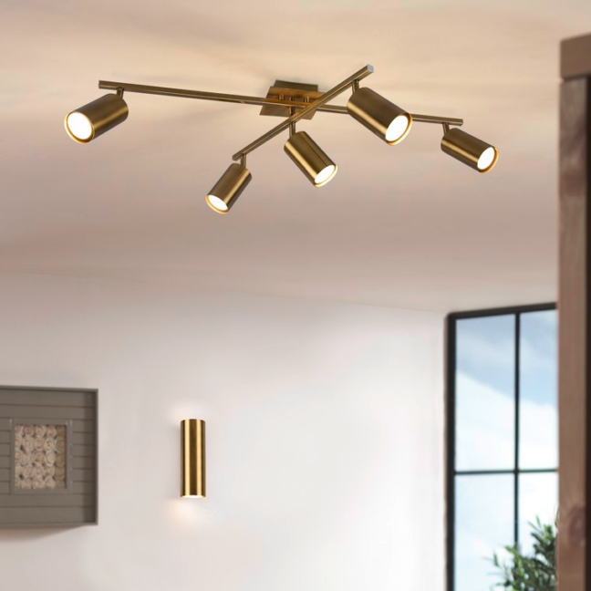 Nowoczesna złota lampa sufitowa Marley 5 typu spot z pięcioma regulowanymi reflektorami LED na krzyżujących się ramionach, wisząca w jasnym salonie obok pasującego złotego kinkietu, idealna do oświetlenia punktowego przestrzeni dziennej