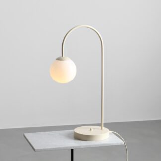 Stołowa lampa Una w kremowym kolorze – kulisty klosz na łukowatej podstawie